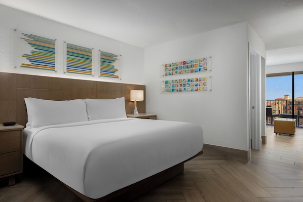 Habitación de hotel con una cama grande, cabecera de madera, mesita de noche y una lámpara, además de obras de arte en las paredes.