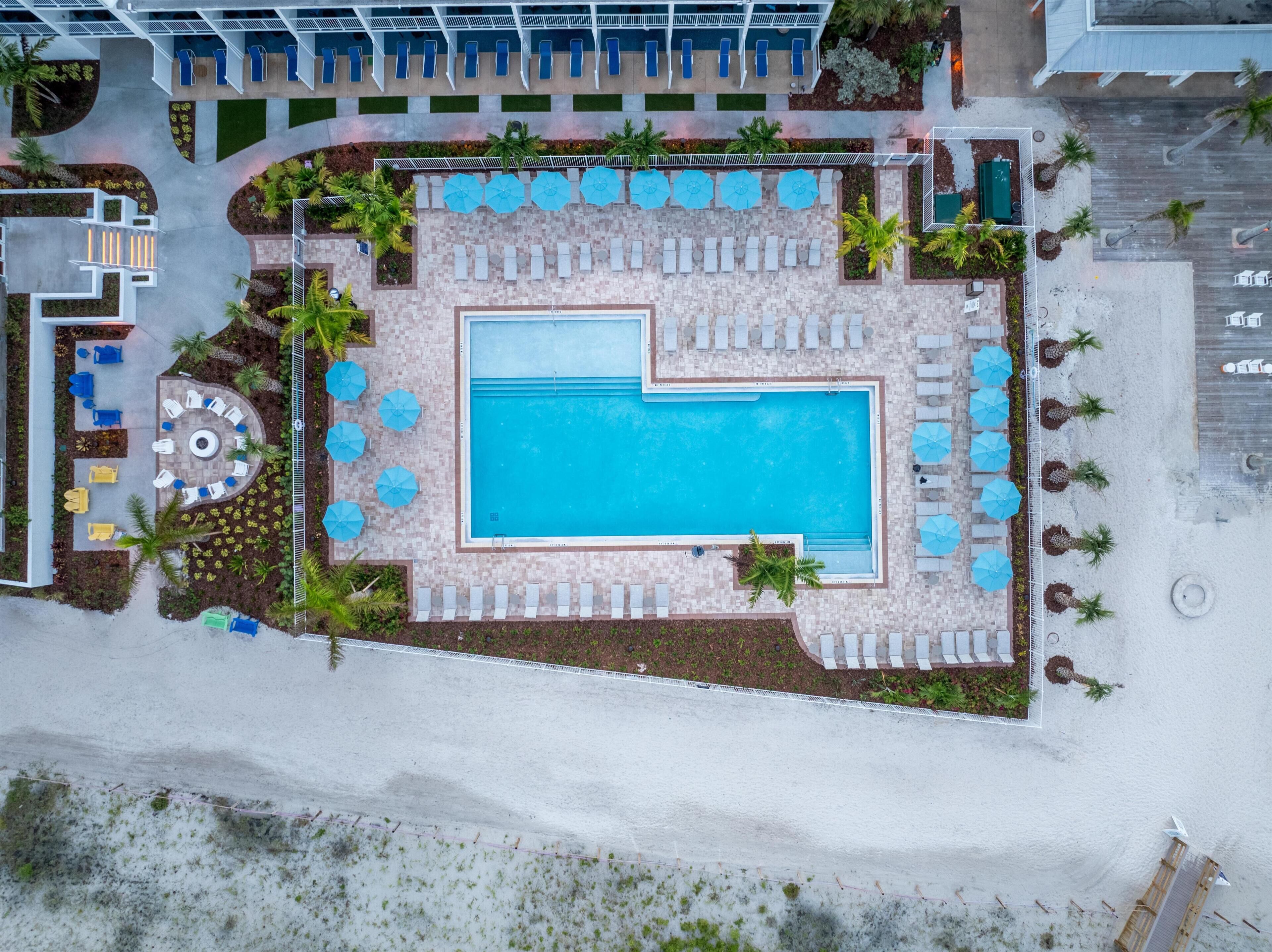 Eine Vogelperspektive auf einen Hotelpoolbereich mit rechteckigem Pool, Liegestühlen, Sonnenschirmen und Palmen.