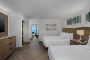 Habitación de hotel con dos camas, un escritorio, una silla, un televisor y vista al océano.