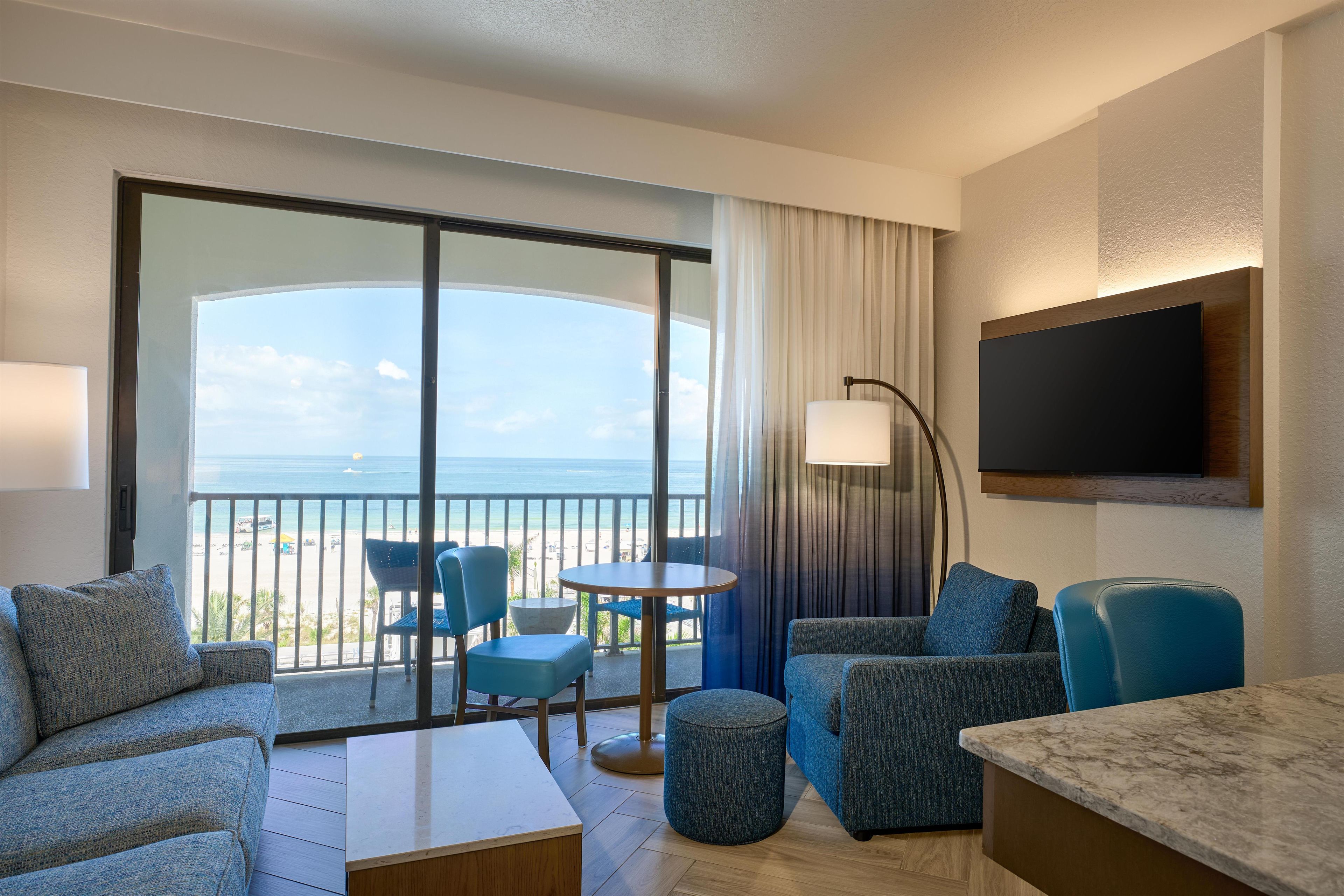A hotel room with a balcony, a flat-screen TV, and a seating area with a table and chairs.