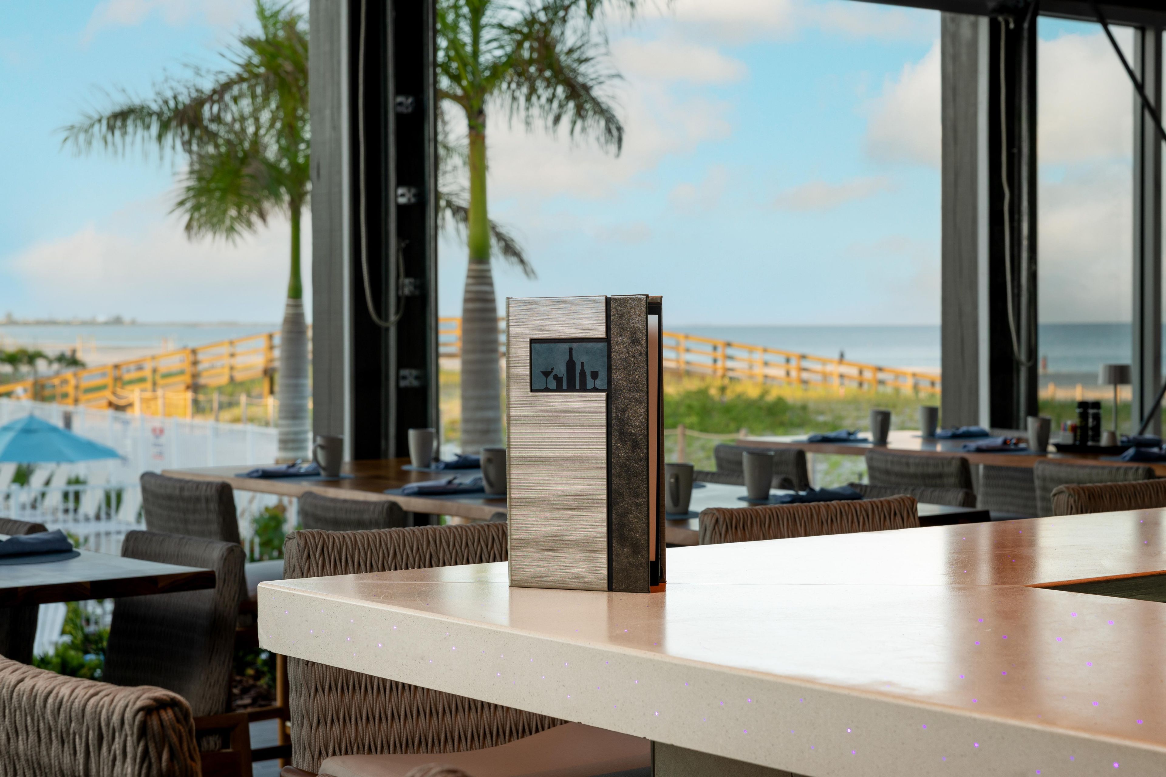 Zona de bar moderna con vistas a la playa y palmeras.