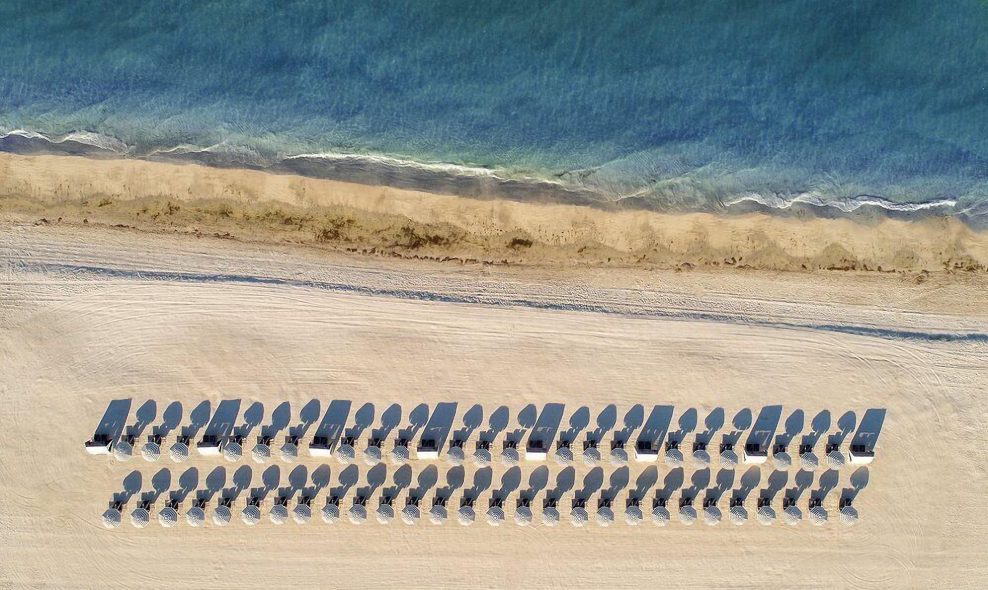 A beach with rows of sun loungers aligned parallel to the shoreline.