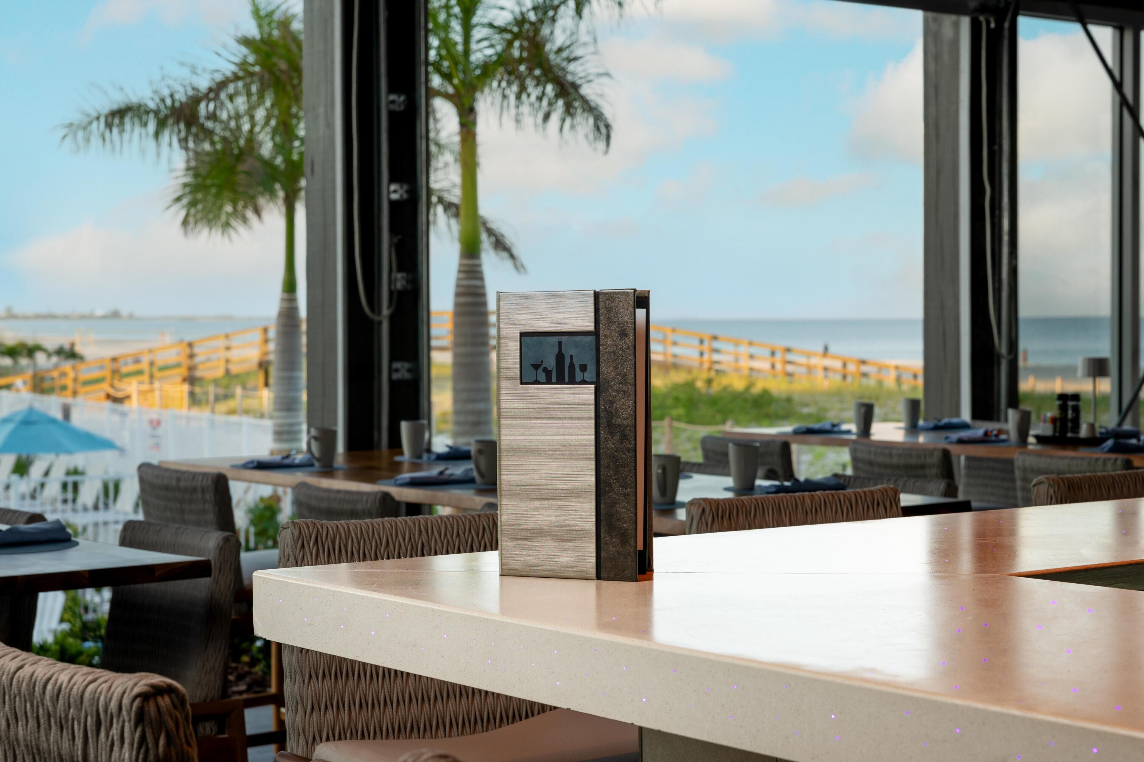 A modern bar area with a view of the beach and palm trees.