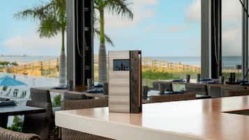 A modern bar area with a view of the beach and palm trees.