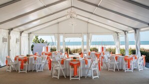 Un salón de bodas con carpas, mesas y sillas, una araña de cristal y vistas a la playa.