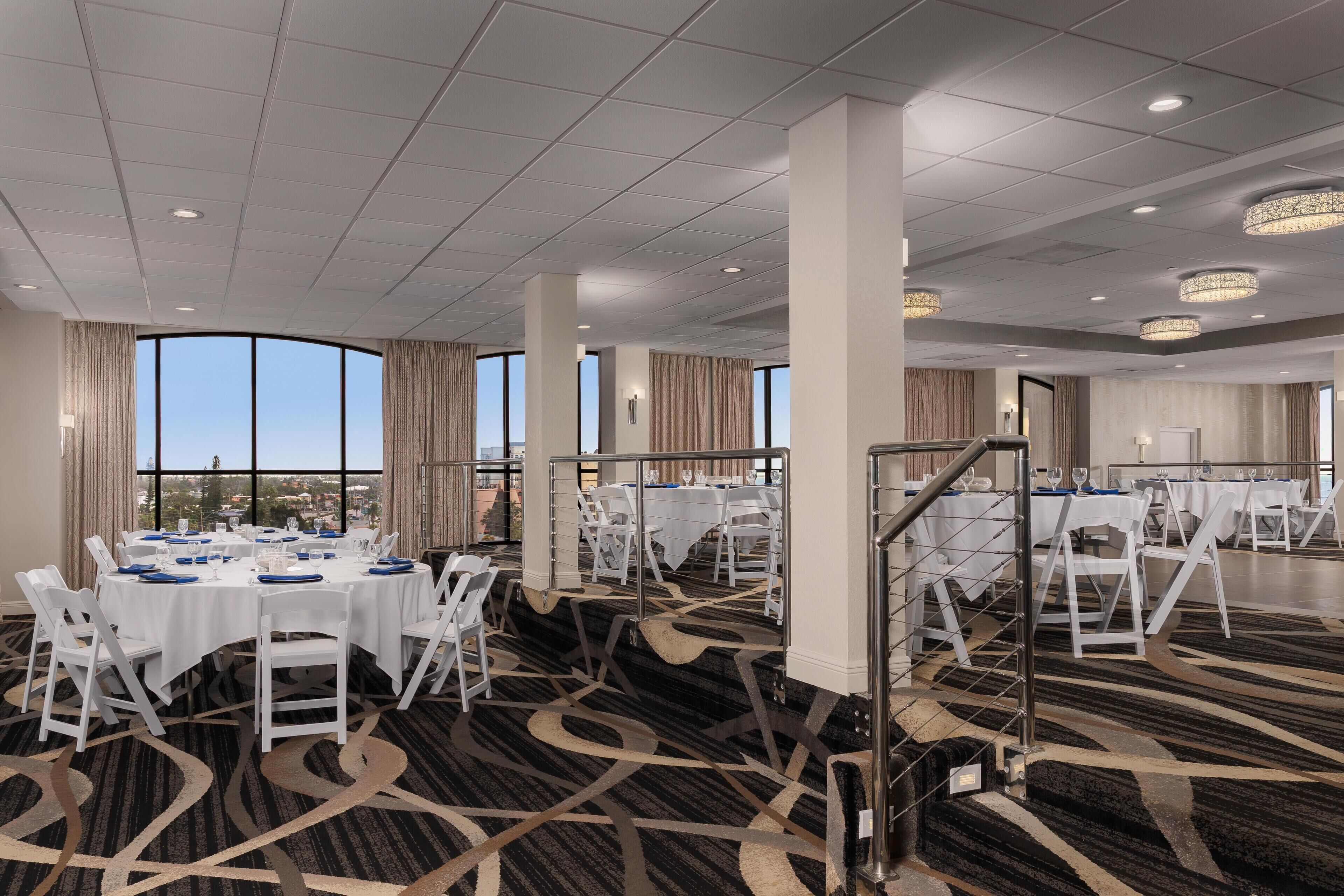 A spacious conference room with multiple tables set for dining, large windows offering a view, and a patterned carpet.