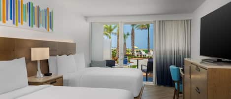 A hotel room with two beds, a desk, a television, and a view of palm trees and a pool.