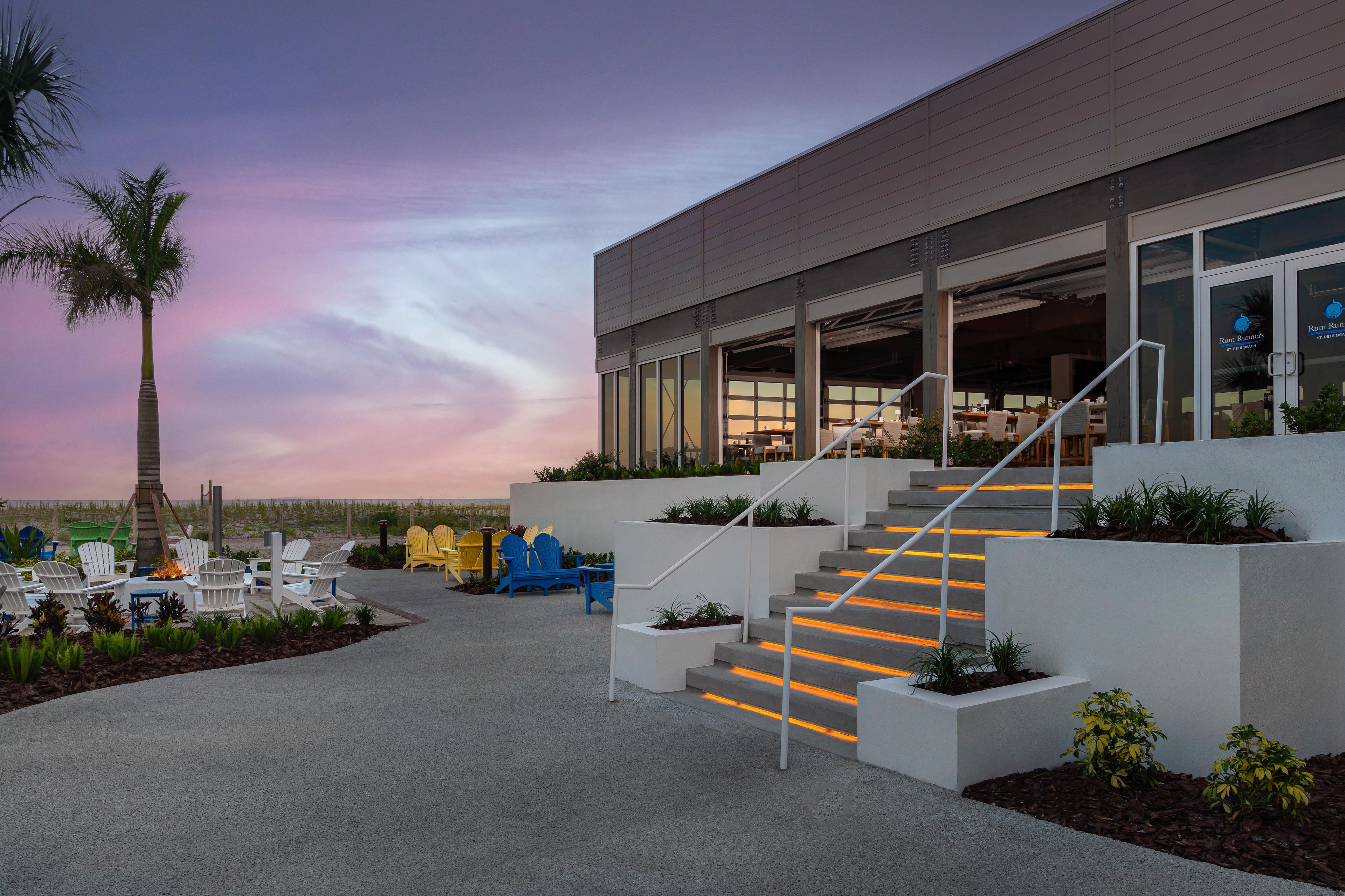A modern building with a staircase leading to an outdoor seating area with chairs and a fire pit.