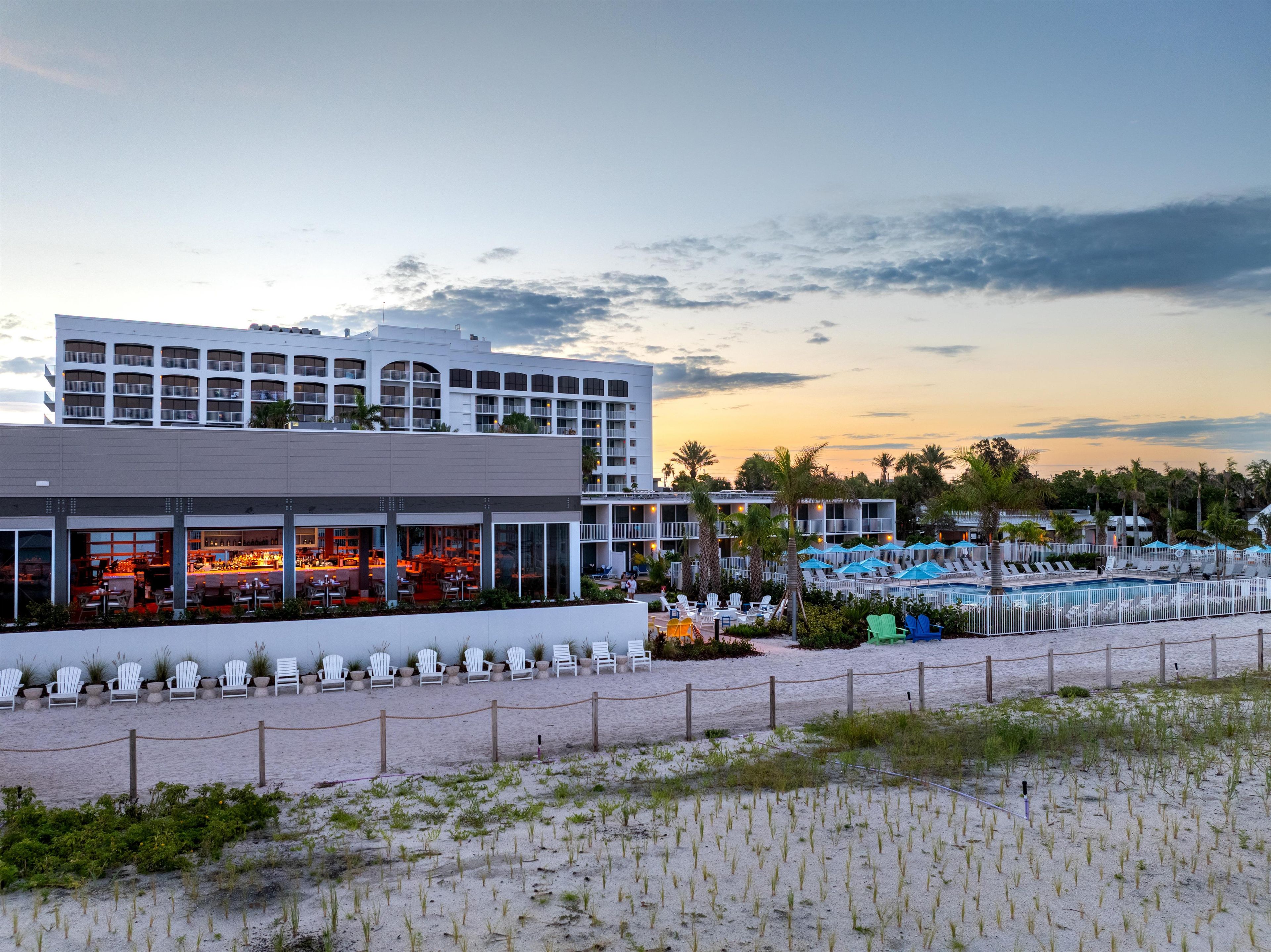 Un hotel con varios pisos, mesas al aire libre y un área de piscina.