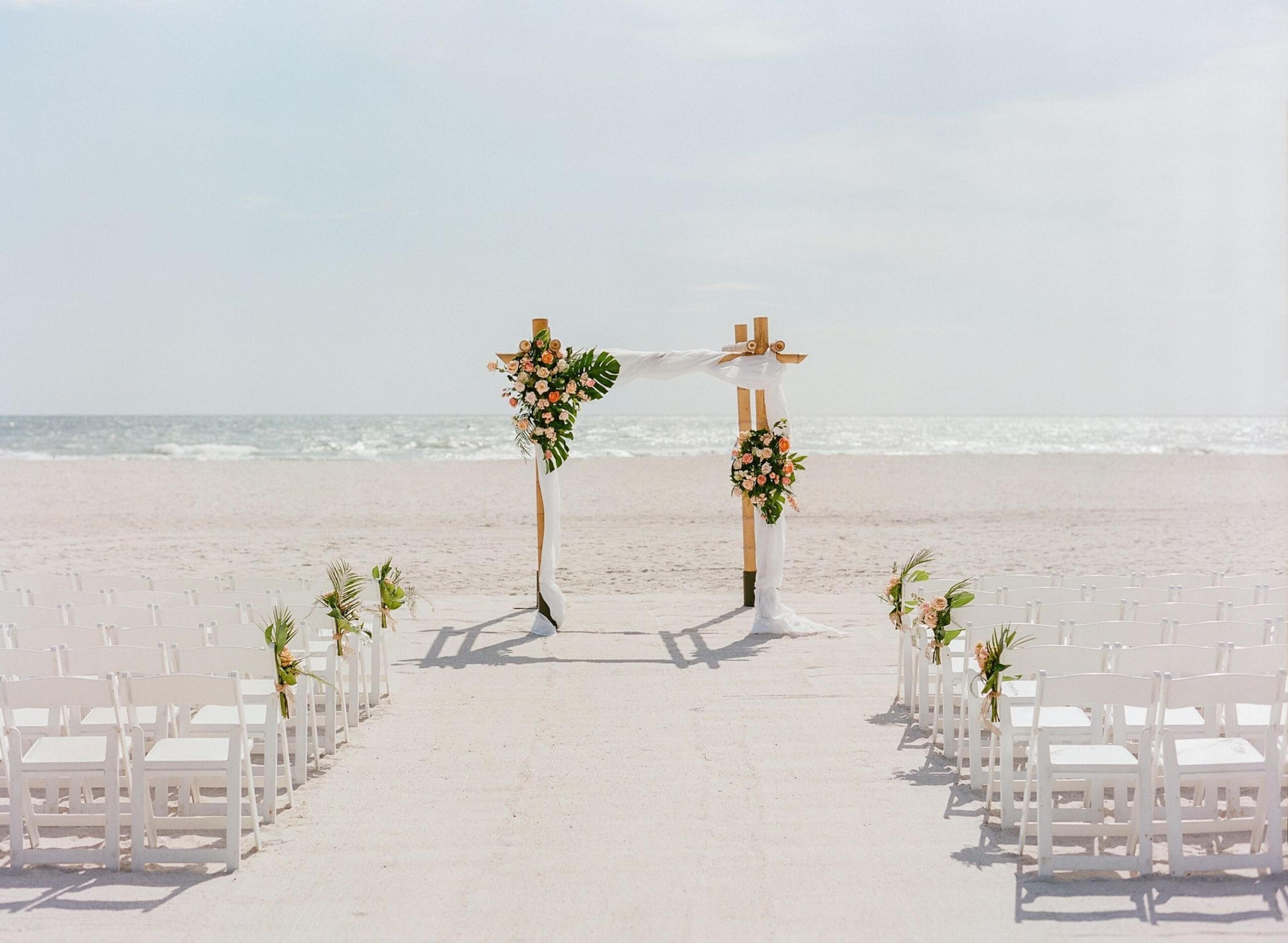 A beach wedding setup with white chairs and floral decorations.