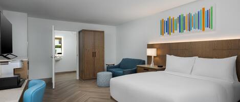 Une chambre d’hôtel comprenant un lit, un bureau avec un ordinateur, une chaise, une armoire et une œuvre d’art murale.