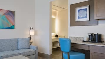 A hotel room with a sofa, a chair, a coffee maker, and a framed picture on the wall.