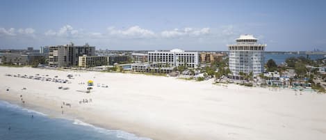 Un resort frente a la playa, con una extensa playa de arena, una alta torre de observación y varios edificios con balcones con vistas al mar.