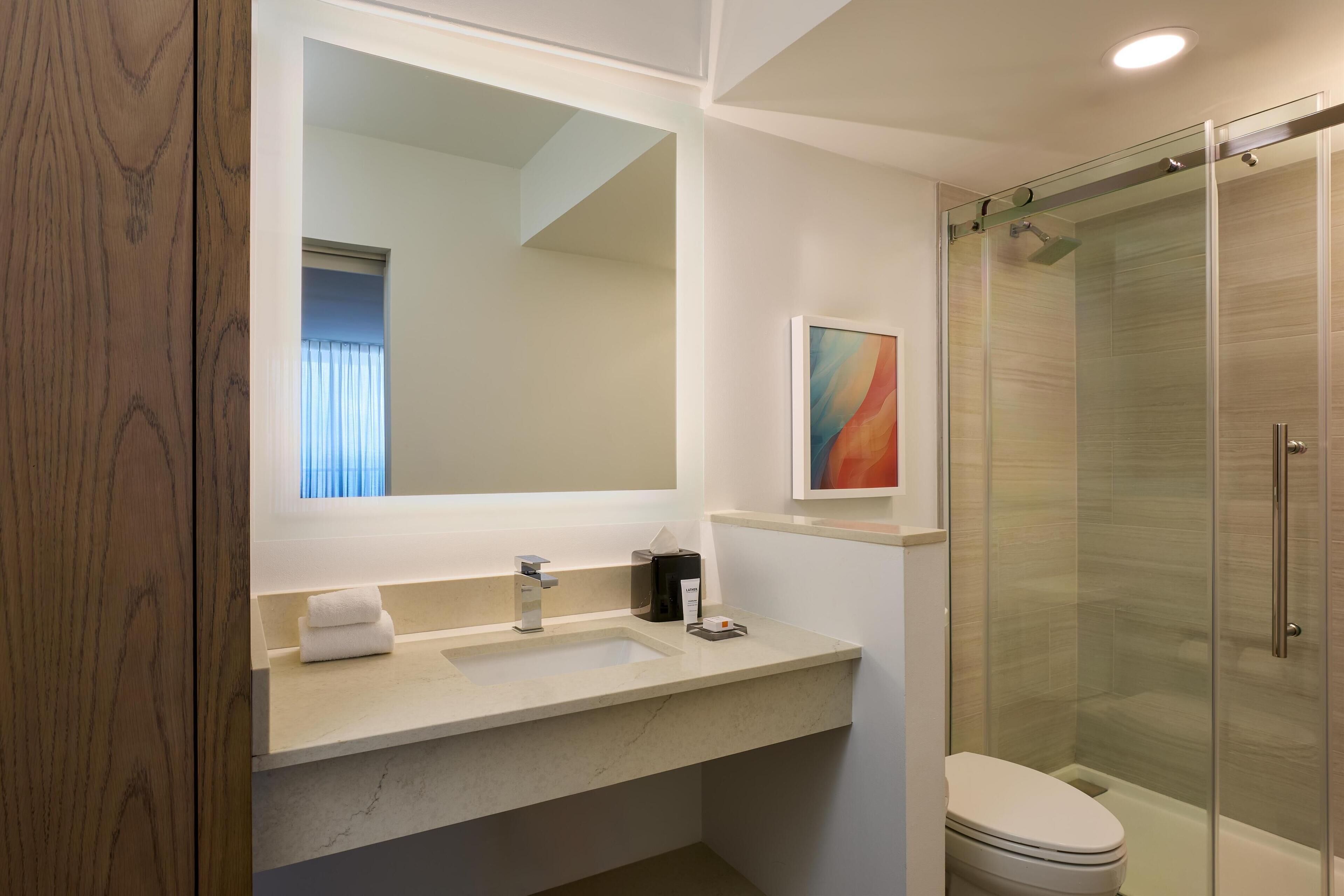 Une salle de bain moderne avec un grand miroir, un lavabo avec une serviette, une machine à café et une douche à parois de verre.