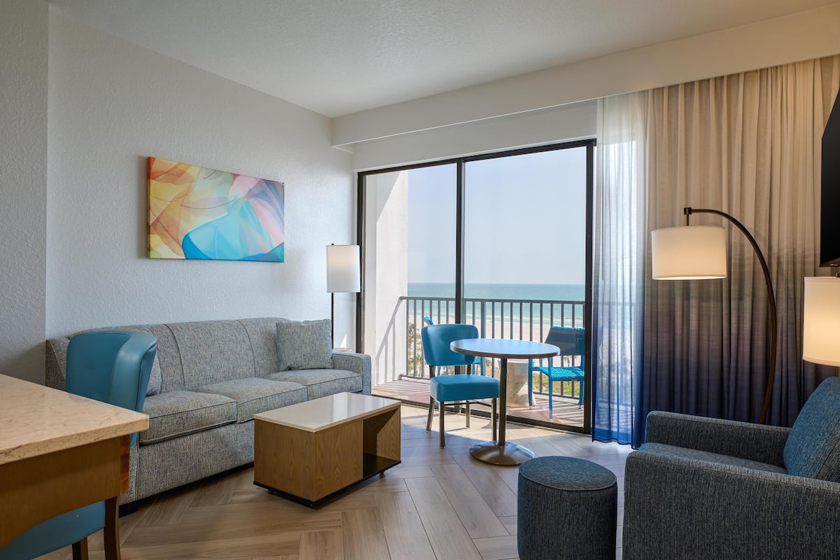 Una habitación de hotel moderna con balcón, un sofá, una mesita de centro y una mesa de comedor.