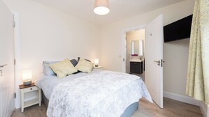 Une chambre à coucher comprenant un lit, des tables de chevet, une commode, une lampe, un miroir et une porte donnant sur une salle de bain.