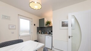 Une cuisine compacte avec un coin repas, comprenant un réfrigérateur blanc, un évier et un petit plan de travail avec une bouilloire et une plante.