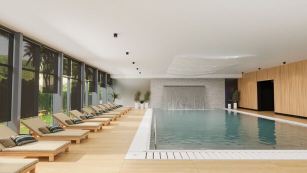 A modern indoor swimming pool with lounge chairs and a waterfall feature.
