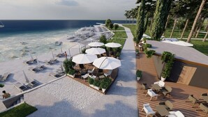 A beachside resort with sun loungers, umbrellas, and a dining area overlooking the sea.
