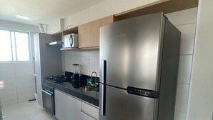 A modern kitchen with stainless steel appliances, white cabinetry, and a window providing natural light. - Edificio Promenade II - Apto 1101 (Maceió)