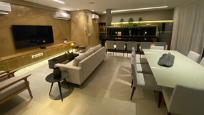 A modern living room with a sofa, TV, dining table, and chairs. - Edificio Promenade II - Apto 1101 (Maceió)