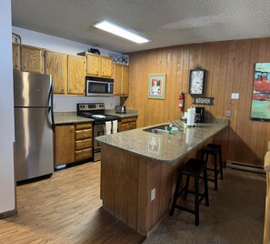 Kitchen area with a refrigerator, stove, microwave, and toaster, plus a small island with bar stools.