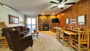 A cozy living room with a stone fireplace, wooden furniture, and a ceiling fan. - Unit 114 - Updated Condo (Winter Park)