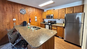 A kitchen with wooden cabinets, a stainless steel refrigerator, a microwave, a stove, and a sink. - Unit 114 - Updated Condo (Winter Park)
