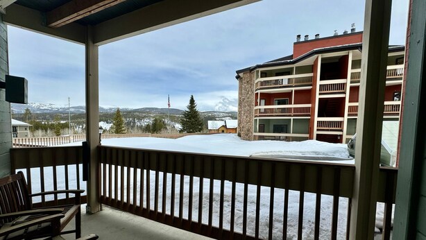 A covered balcony with a view of a snow-covered landscape, a multi-story building, and a flag. - Unit 114 - Updated Condo (Winter Park)