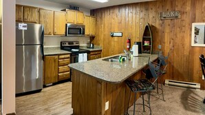 A kitchen with wooden cabinets, a stainless steel refrigerator, a microwave, a stove, and a granite countertop. - Unit 212 - Standard Condo (Winter Park)