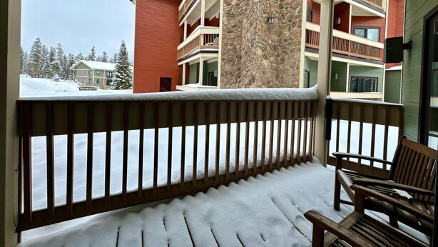 A balcony with a wooden railing, a bench, and a view of a multi-story building with a stone facade. - Unit 212 - Standard Condo (Winter Park)