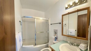 Et badeværelse med bruser, toilet, håndvask og et stort spejl.