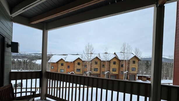 A wooden deck with a railing, a bench, and a view of a row of wooden houses with snow on the ground.