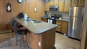 A kitchen with wooden cabinets, a granite countertop, stainless steel appliances, and a clock on the wall.