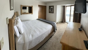 A hotel room with a bed, a desk, a TV, a window, and a door.