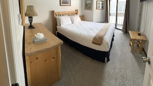 Un dormitorio con cama, mesita de noche, lámpara y televisor montado en la pared.