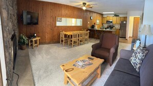 Una sala de estar con una mesa de comedor de madera, un sofá, una mesa baja y un televisor.