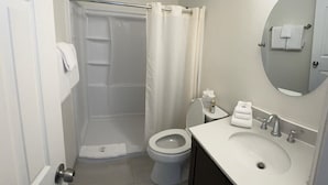 Baño con ducha, inodoro, lavamanos y espejo.