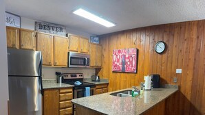 A kitchen with wooden cabinets, a stainless steel refrigerator, a microwave, an oven, a sink, and a clock on the wall. - Unit 512 - Updated Condo (Winter Park)