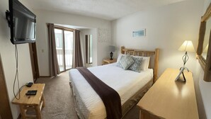 A hotel room with a bed, a TV mounted on the wall, a desk with a lamp, and a small table with a remote control. - Unit 512 - Updated Condo (Winter Park)