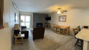 Ein Wohnzimmer mit Kamin, einem Essbereich mit Holzsesseln, einer Couch und einem an der Wand montierten Fernseher.
