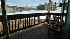 En træterrasse med en bænk, med udsigt over et sneklædt landskab og bygninger.
