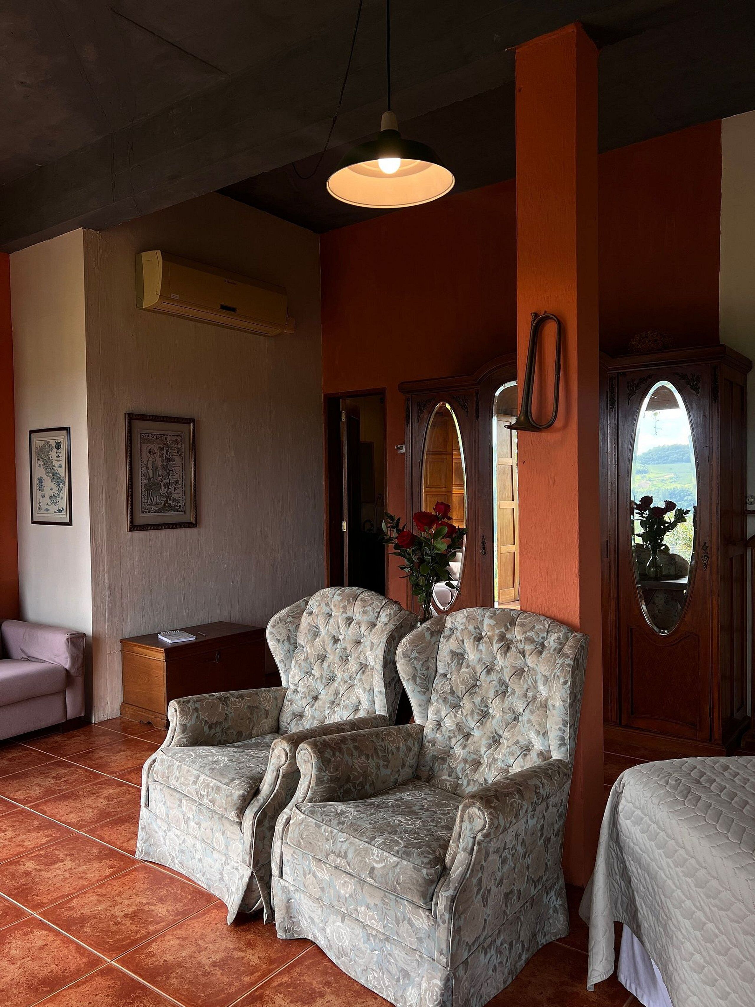 Quarto com duas poltronas estofadas, um armário de madeira e um espelho grande.