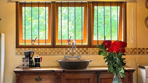 A kitchen with wooden cabinets, a sink, a dining table, and a vase with red roses. - Pousada Borghetto (Bento Gonçalves)