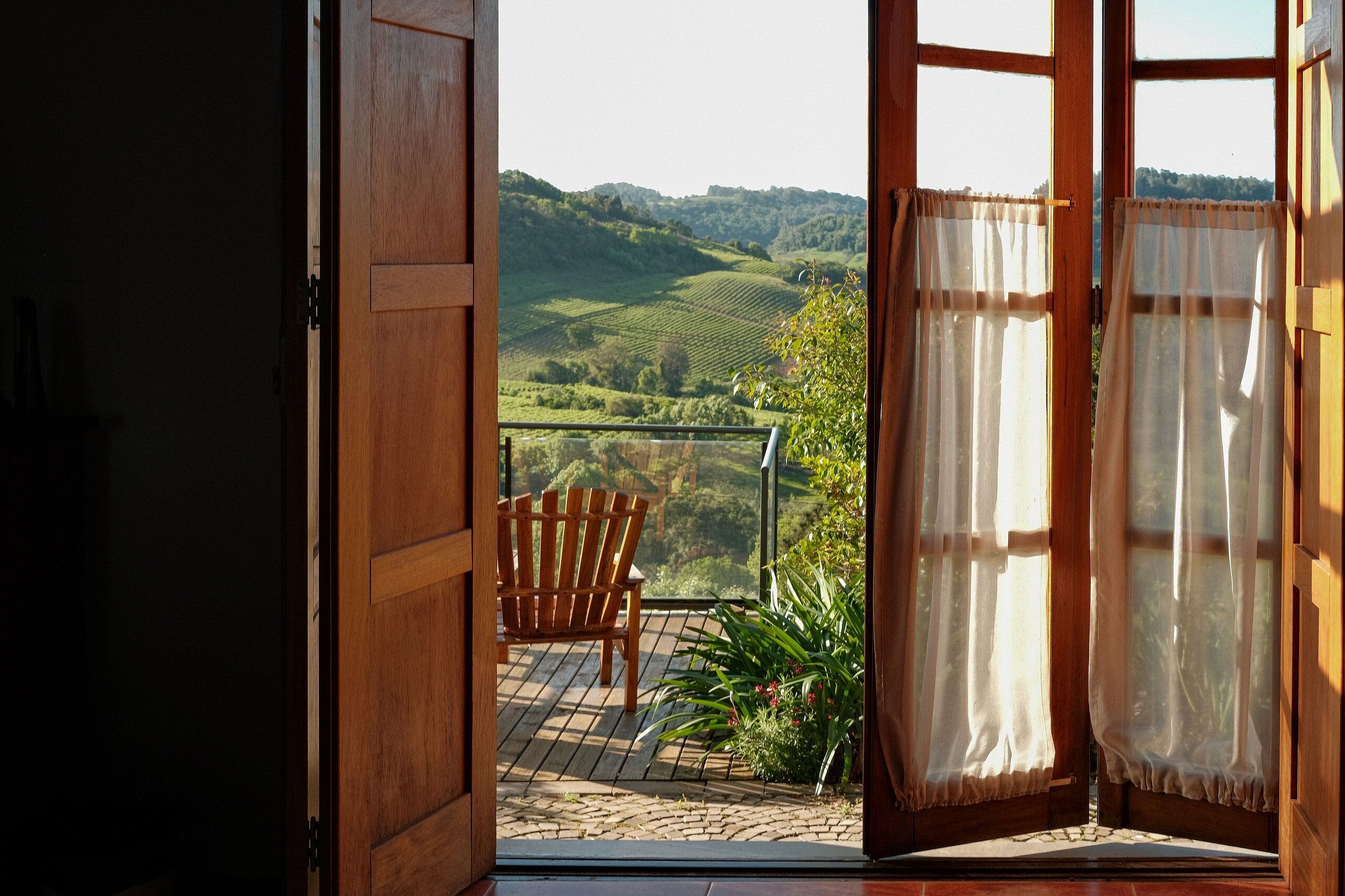 An open wooden door leading to a balcony with a chair and potted plant.