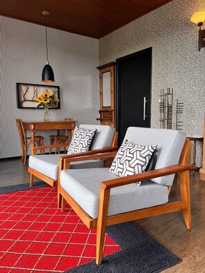 Una sala de estar moderna con un sofá, sillas, una mesa de comedor y un tapete estampado en rojo y negro.