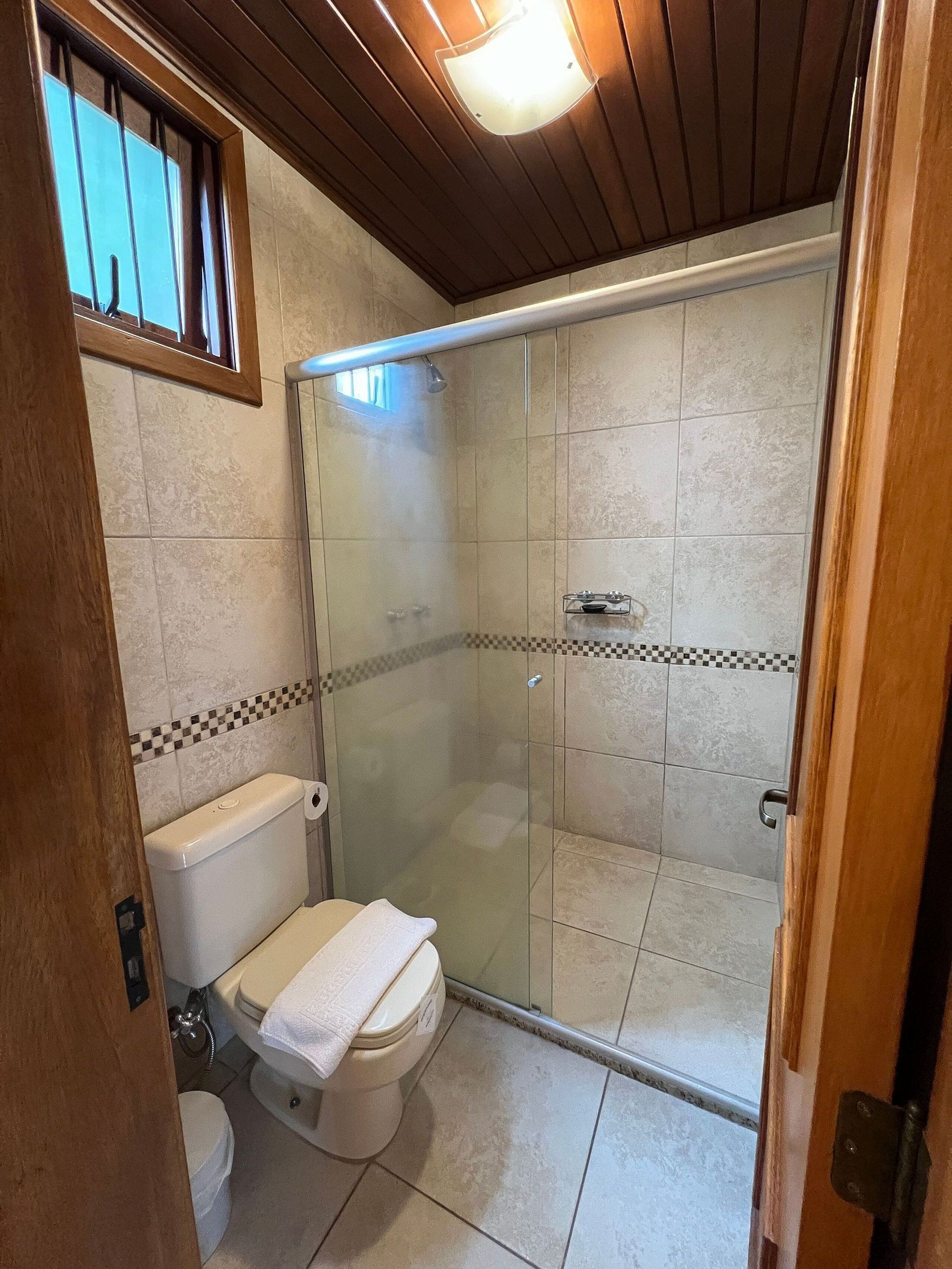 Um banheiro com vaso sanitário, chuveiro com box de vidro e piso revestido de azulejos.