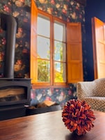 Una habitación con una mesa de madera, una piña, una chimenea y una ventana con papel tapiz floral.