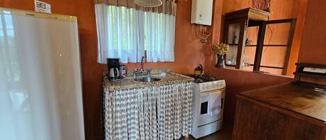 A compact kitchen with a refrigerator, stove, sink, and a coffee maker.