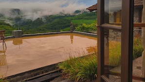 A view from a window overlooking a rooftop terrace with a paved area, a chair, and a stone wall. - Pousada Borghetto (Bento Gonçalves)
